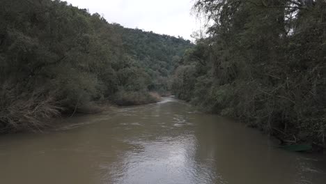 Low-aerial-view-over-a-small-flowing-river-in-the-middle-of-the-dense-Paranaense-jungle-in-Misiones,-Argentina