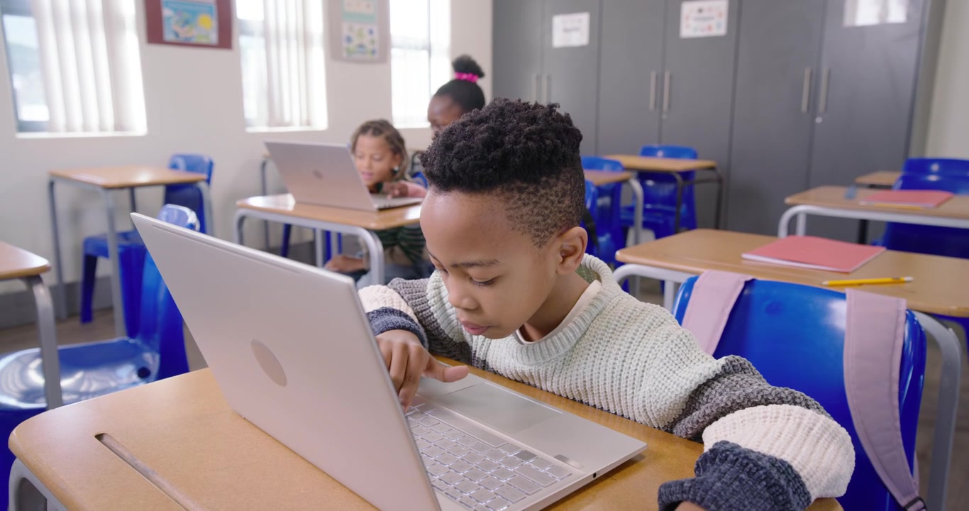 Studenti di diverse etnie al lavoro, un ragazzo afroamericano che osserva il laptop, si china e digita mentre svolge un compito in classe
