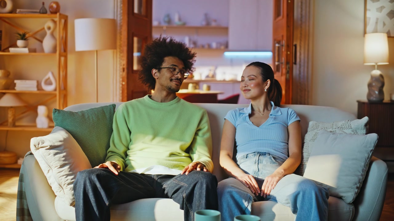 Multiethnic pair breathing exercise sofa. Relaxed man woman smiling living room.