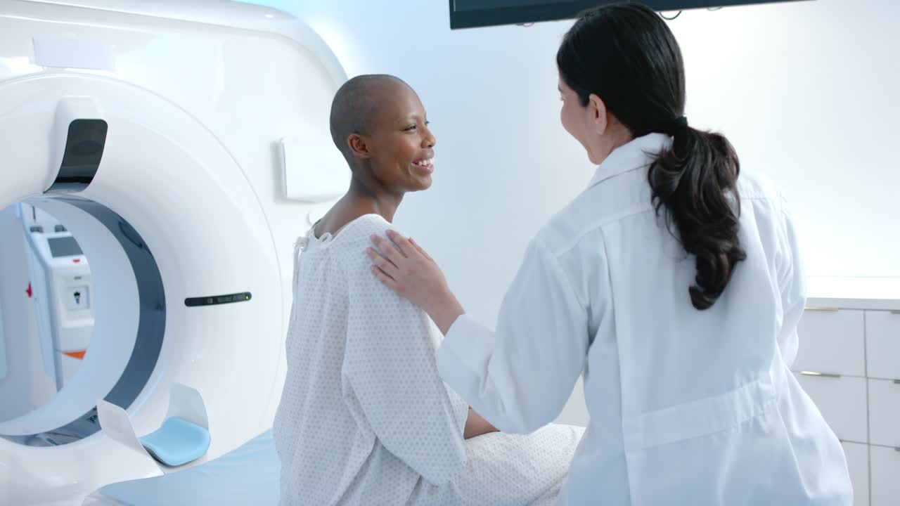 Una dottoressa appoggia una mano sulla spalla di una paziente seduta al lettino medico vicino allo scanner, rassicurandola. La paziente sorride.