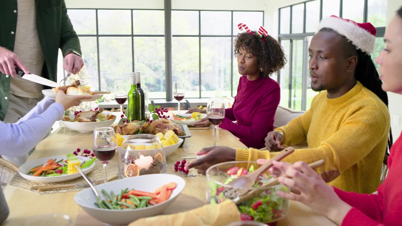 Groupe diversifié réuni autour d’une table pour un repas de fête, préparant la salade, découpant la dinde, levant leurs verres