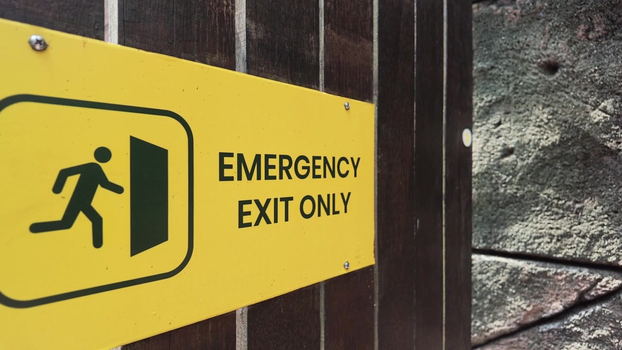 Panneau jaune "Sortie de secours uniquement" monté sur une porte en bois