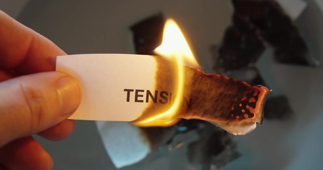 Primo piano di una striscia di carta con la parola “tensione” che brucia, a simboleggiare stress, pressione, conflitto, tensione emotiva e liberazione da sentimenti negativi.