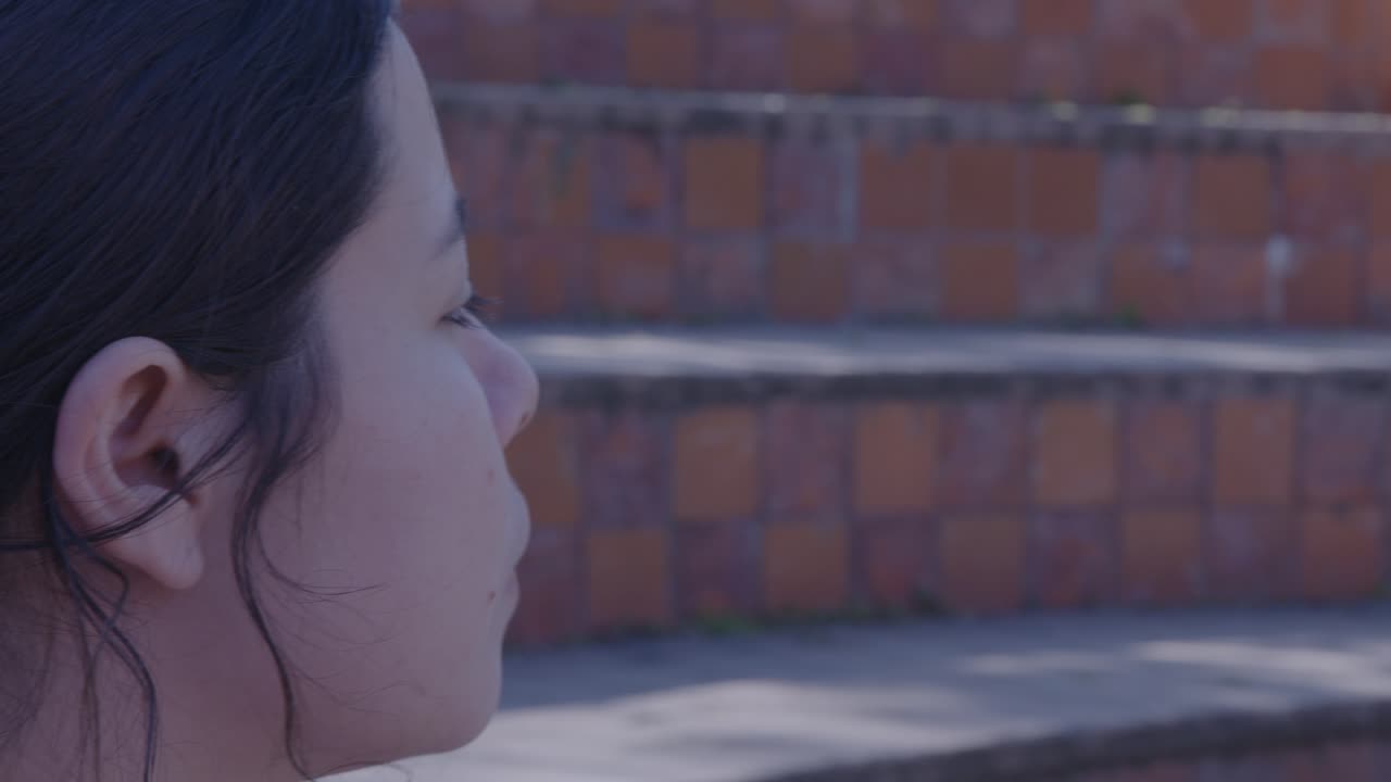 A serene side profile of a woman seated on a sunlit staircase, her hair tied back with a decorative clip, enjoying a moment of quiet reflection. Calm atmosphere and soft lighting