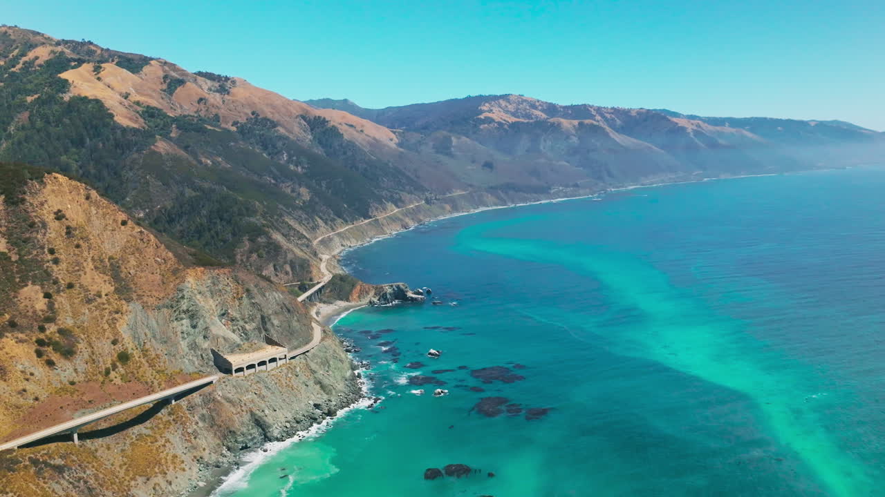 Breath-taking scenery of mountains with some greenery growing on. Turquoise ocean washing the rocky shore. Aerial view.