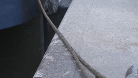 close up of the rope of a small fischer boat floating in the harbor while hanging on a boulder log