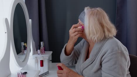 Old-senior-woman-grandmother-putting-makeup-on,-applying-anti-wrinkle-foundation-with-sponge