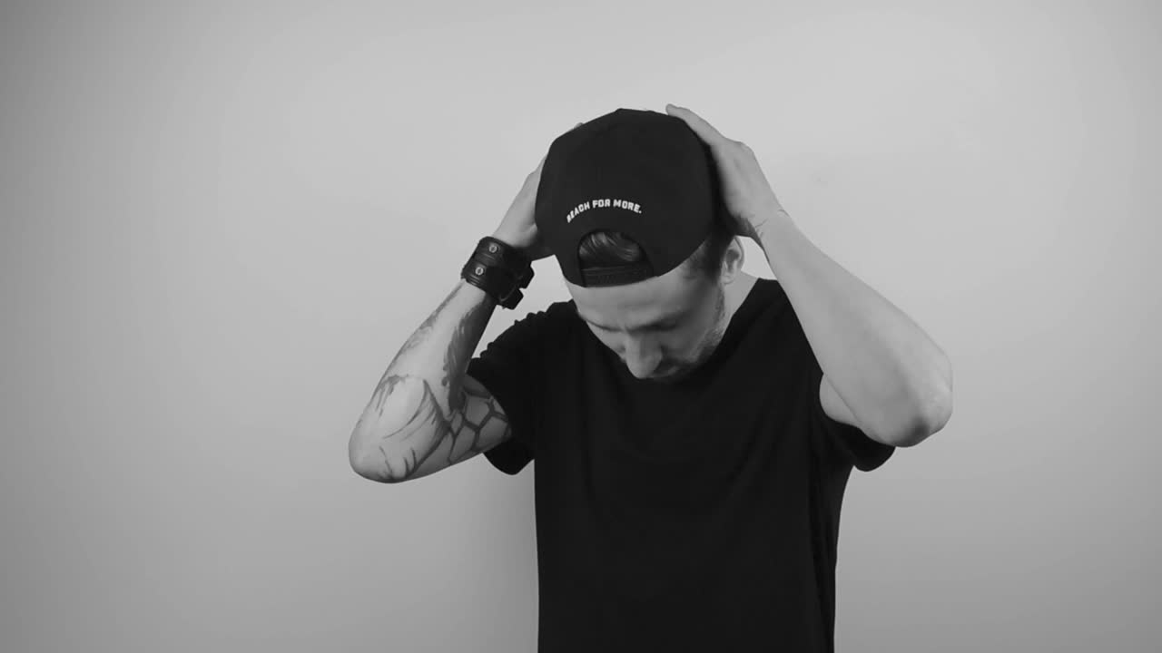 Slow motion video of a tattooed man with a full sleeve tattoo putting on a hat or a cap that is black