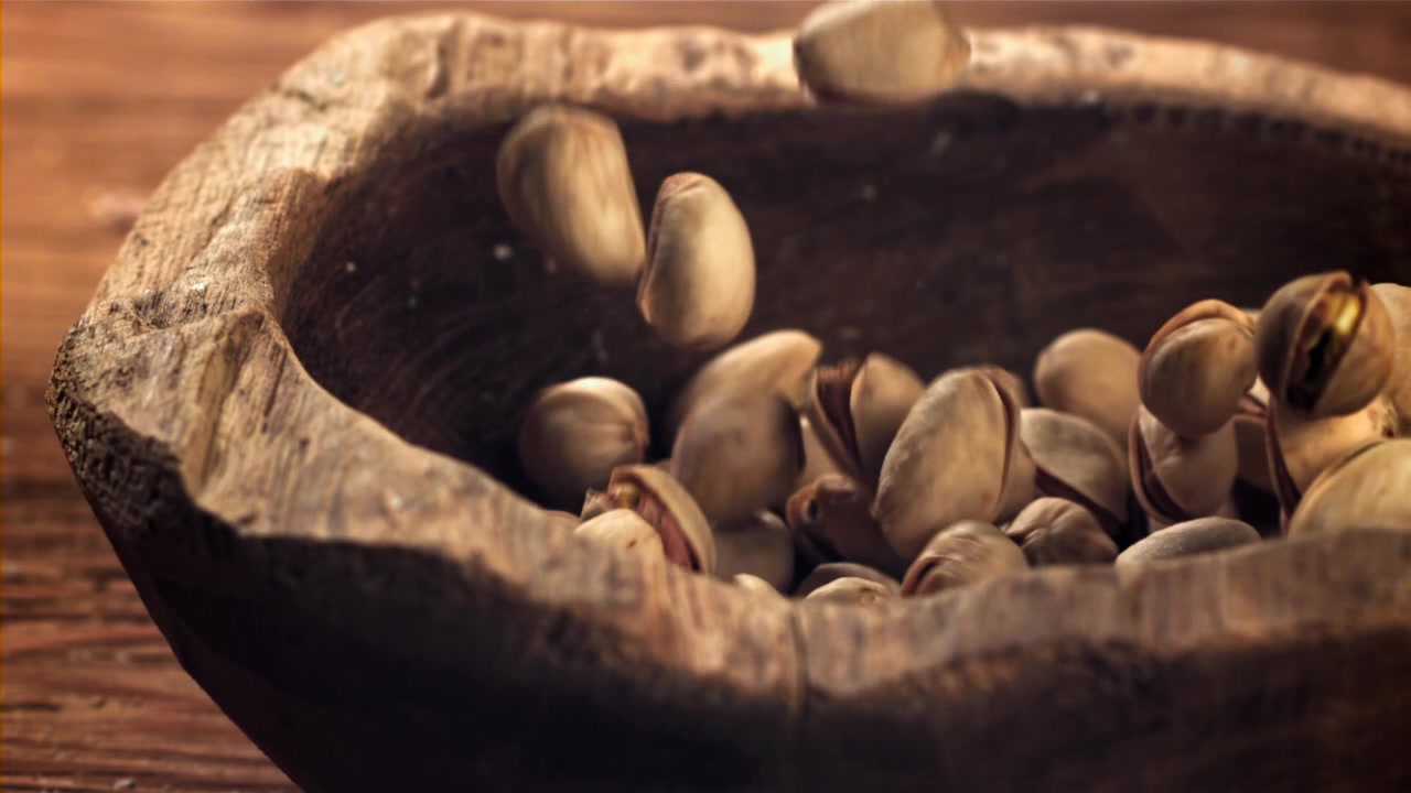Pistachios Falling into a Rustic Wooden Bowl in Slow Motion