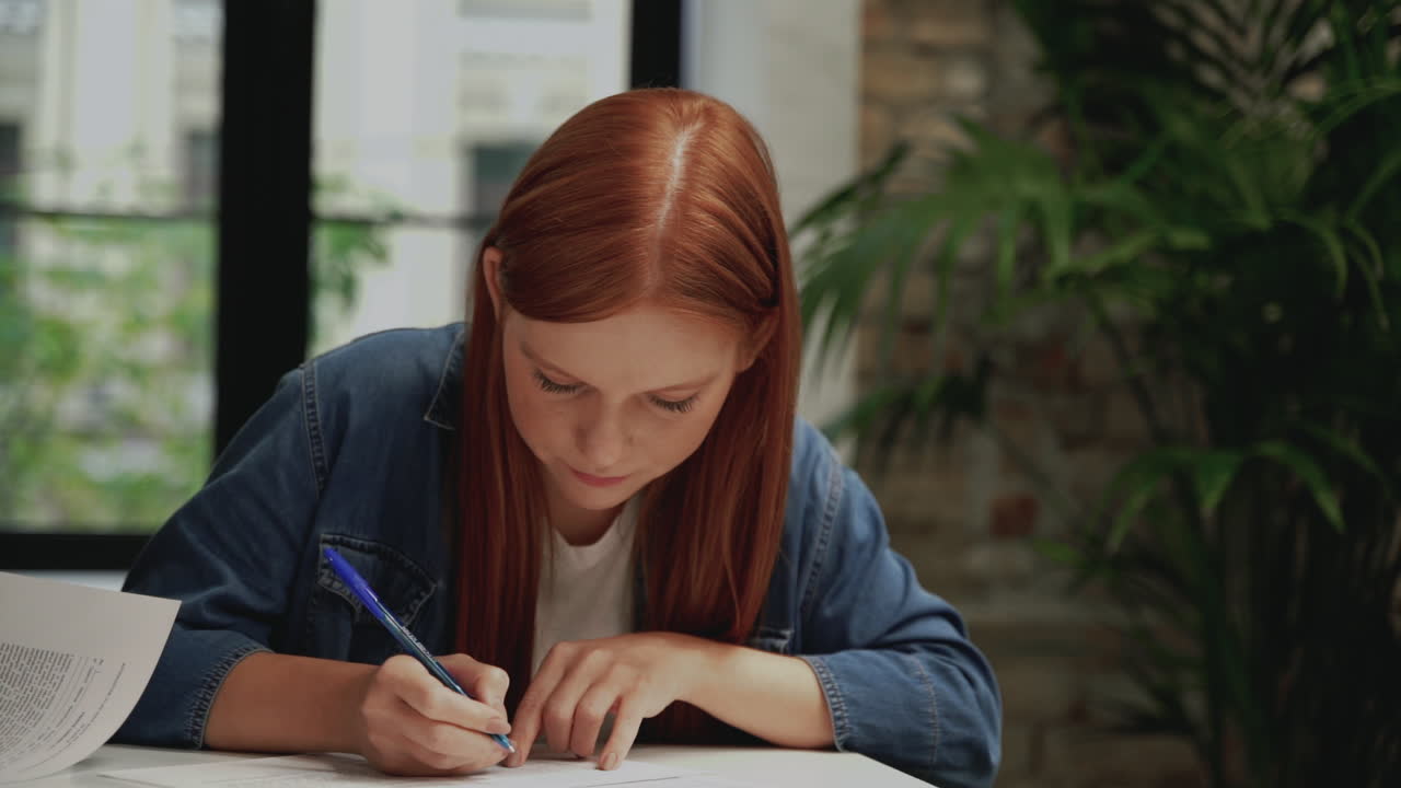 Working woman doing paperwork. Red-haired female filling out an employment contract for a company.