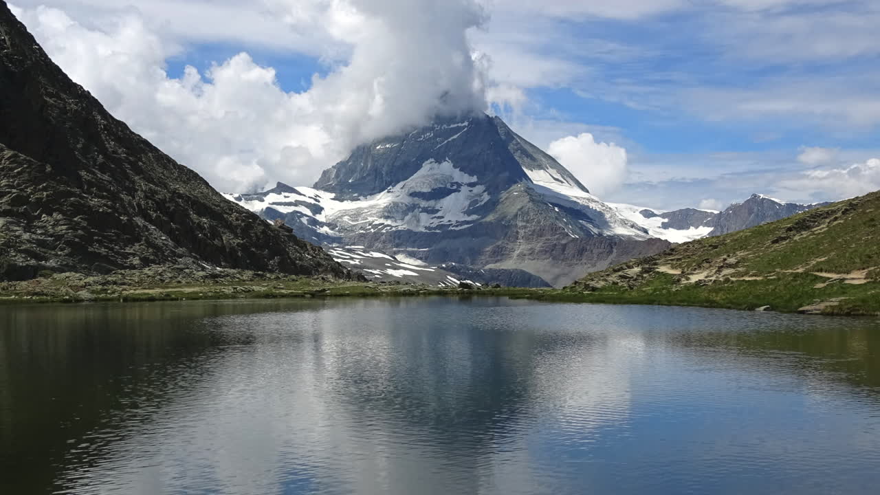 Vista in timelapse di nuvole che fluttuano intorno al Cervino sopra un tranquillo lago alpino e pendii rocciosi a Zermatt, Vallese, Svizzera, suggestivo paesaggio montano estivo.
