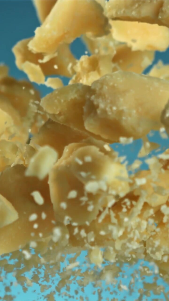 Scaglie di Parmigiano che fluttuano verso l'alto su sfondo blu