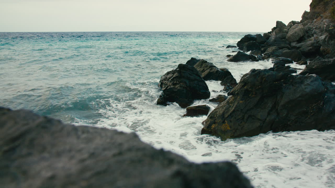 Close-up slow motion footage of ocean wave forcefully hitting jagged rocks on a wild coastal stretch in southern Spain