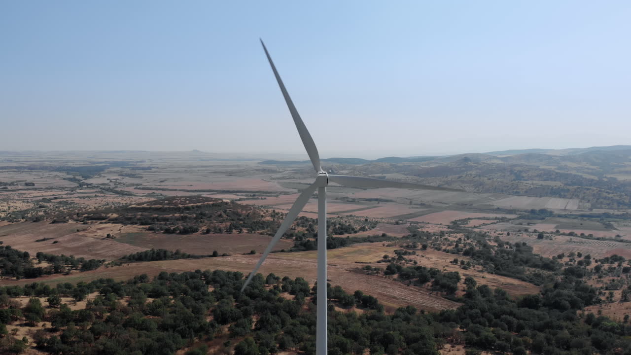 Drone shot behind Wind Turbine Spinning in Rural Area on Sunny Day