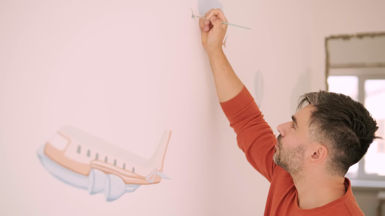 The artist is decorating walls by drawings in the children's room. Art painting of the walls in the new house. Repair works.