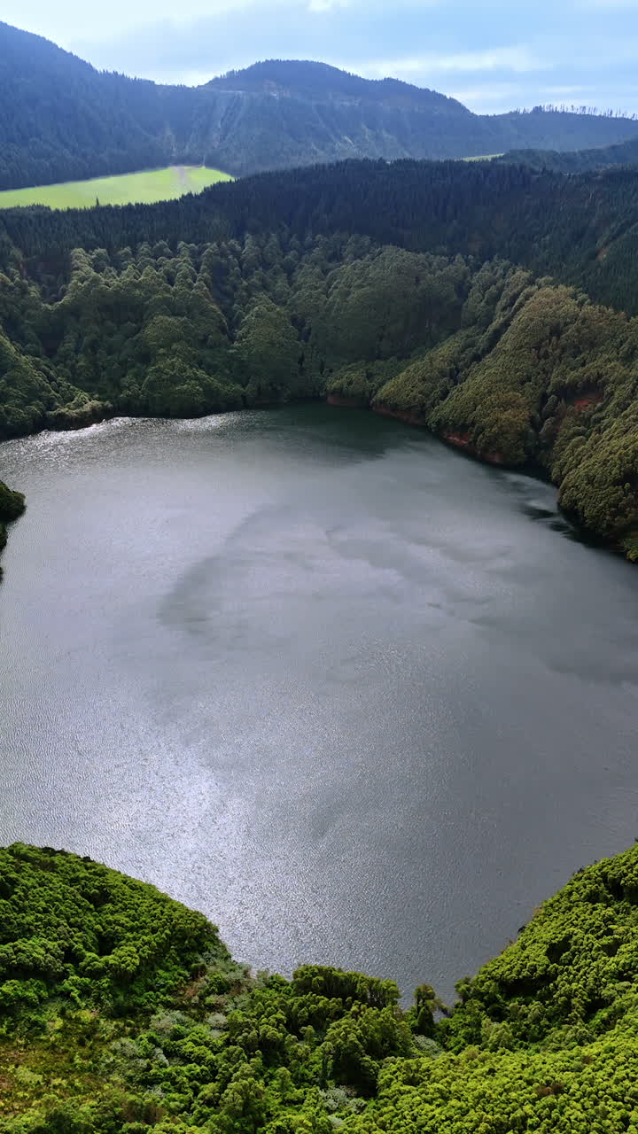 Beautiful small lake inside the mountain overgrown with lush greenery. Stunning nature of the Azorean Islands from top view. Vertical video.