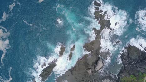 aerial overhead shot of waves of indian ocean hitting boulder and coral reff in the beach in sunny condition weather - pengilon hill, indonesia, asia