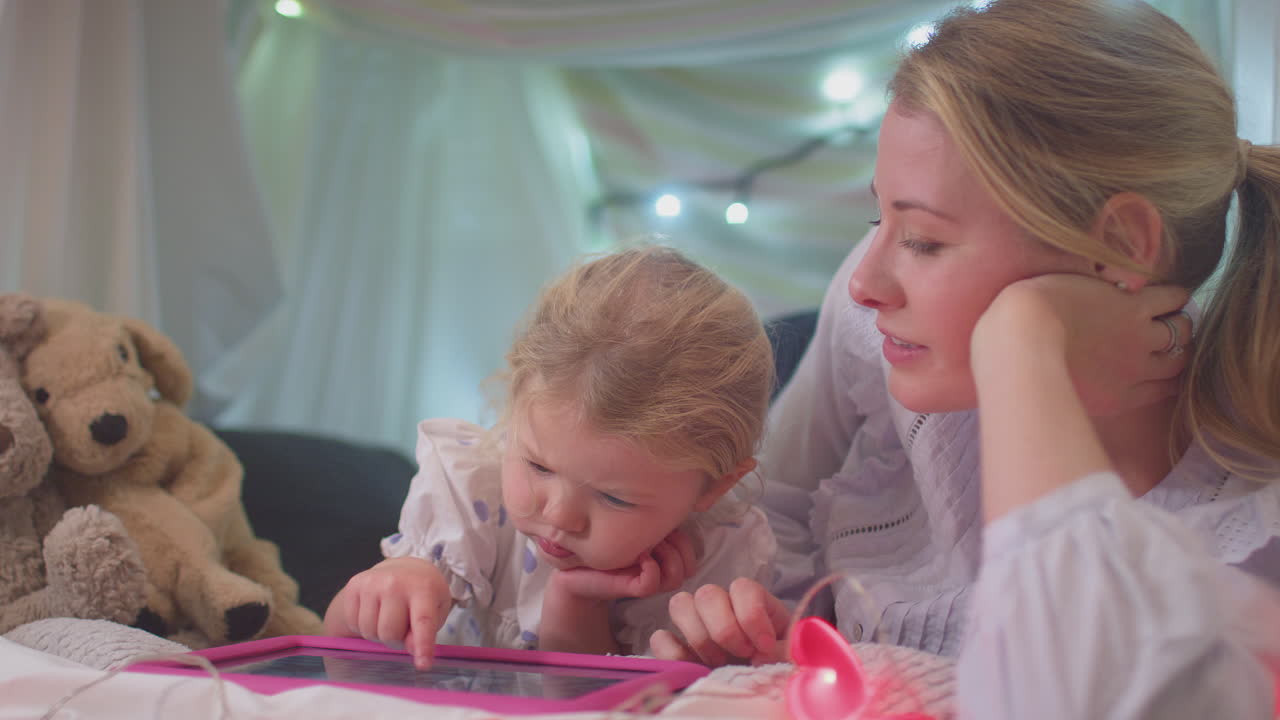 Mother and young daughter with digital tablet in homemade camp in child's bedroom at home - shot in slow motion