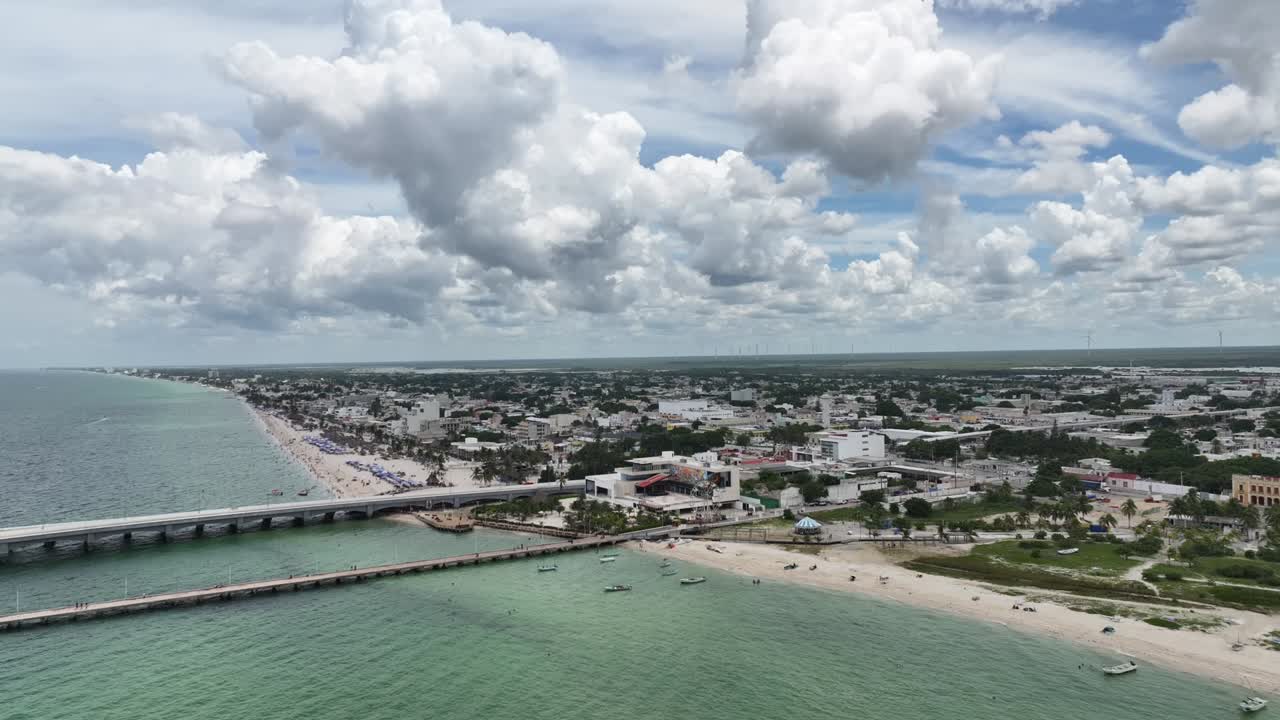 Aerial view of the crowded beach of Progreso, Yucatán, showing turquoise water, umbrellas, and the city under dramatic clouds
