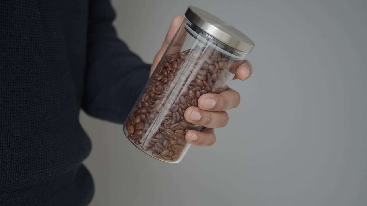Mano sujetando un tarro de cristal con granos de café tostados