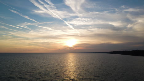 Drone-descends-to-water-as-sun-sets-over-Lake-Erie-spreading-light-across-waves-and-clouds