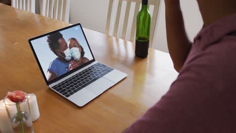 Mid-section-of-african-american-man-drinking-wine-while-having-a-video-call-on-laptop-at-home