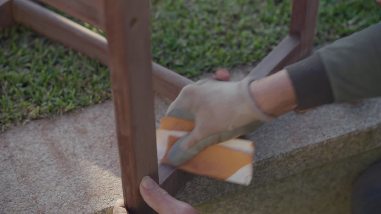Gloved hand sanding wooden frame on stone surface
