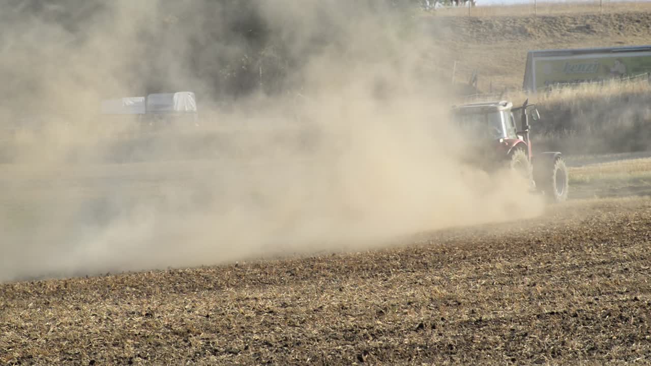 저녁 햇빛에 엄청난 양의 먼지가 있는 독일 시골에서 바위를 단단하고 메마른 들판을 갈고 있는 빨간 트랙터