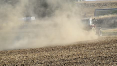 red tractor plowing a rock hard and dried out field in the german countryside with huge amounts of dust in evening sunlight