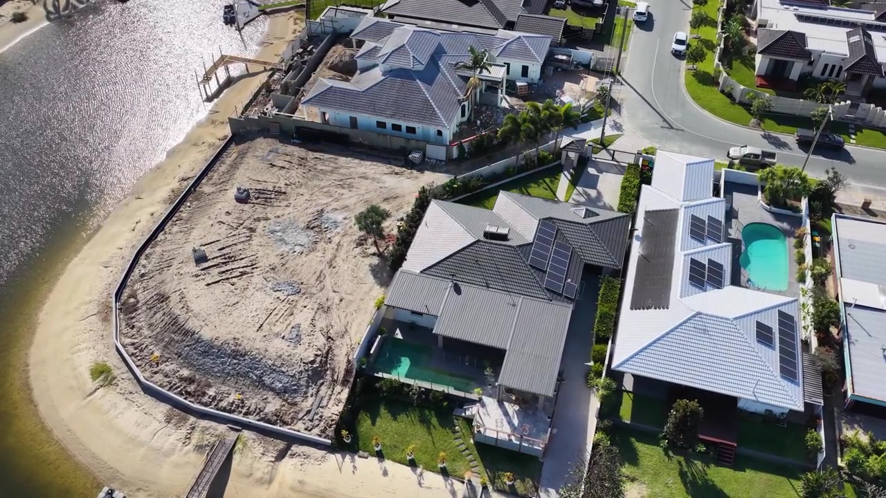 High-angle drone shot reveals upscale canal homes and a vacant lot under development.