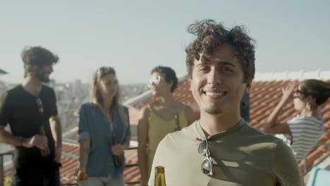 retrato de un joven caucásico mirando la cámara y sonriendo mientras tiene una fiesta en la azotea con amigos