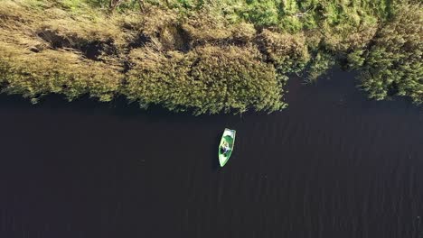 Top-Up-Aufnahme-Mit-Einem-Mann,-Der-Im-Fluss-In-Einem-Fischerboot-In-Der-Nähe-Von-Schilf-Fischt