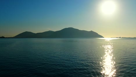 Aerial-establishing-shot-of-seascape-scenery-with-Mountain-silhouette-and-Sun-reflections-on-water-surface