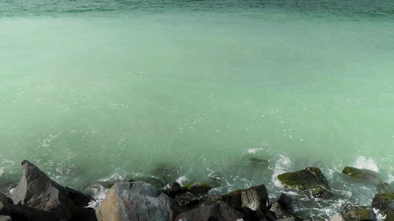 Tilt up shot revealing the sea, waves splashing in the rocky shore and the water having a unique turquoise color