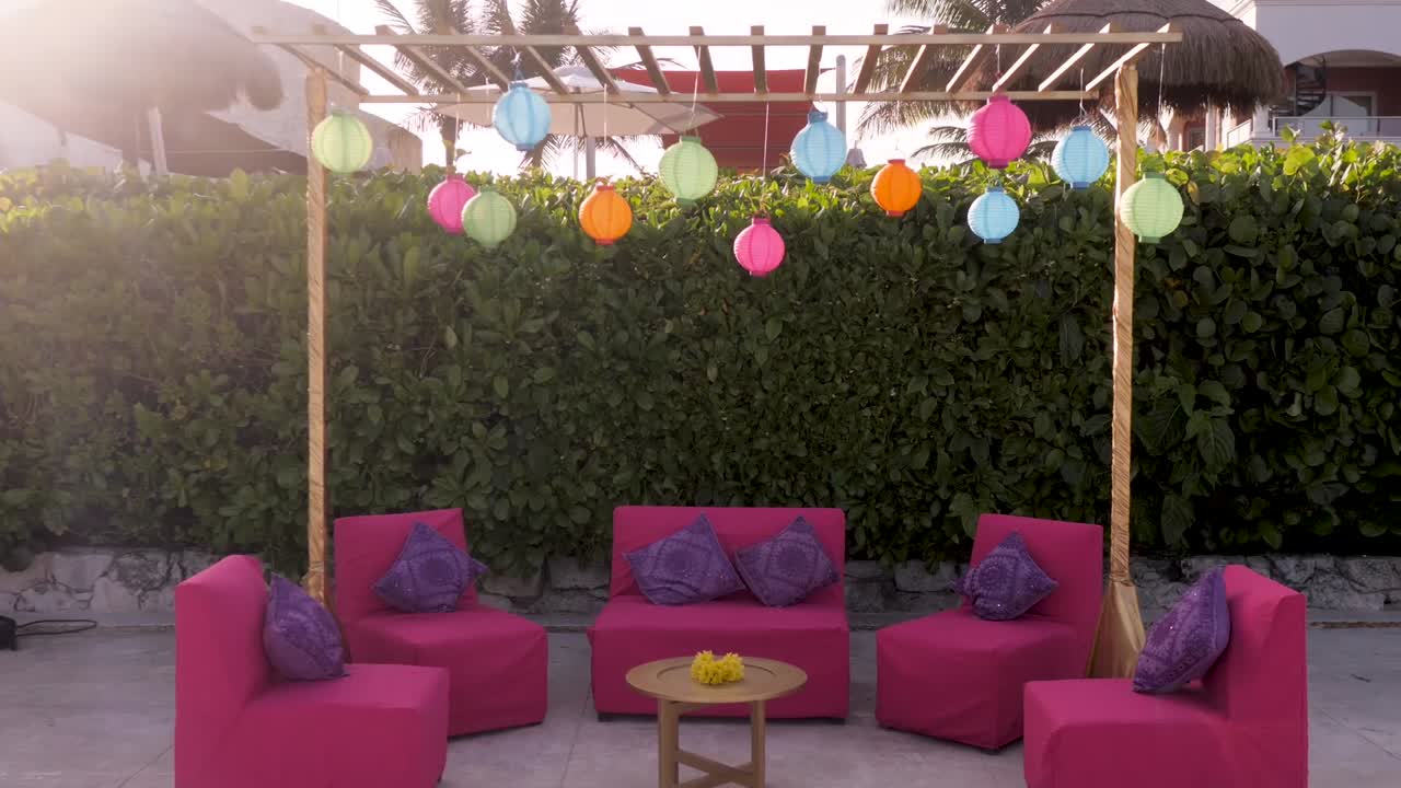 Una toma lateral deslizante de una pérgola decorada con faroles, sofás y una mesa