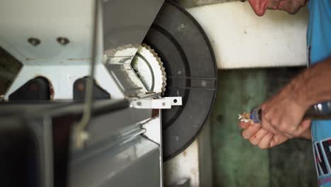 older caucasian wine grower greasing chains of old grape crusher machine in the cellar