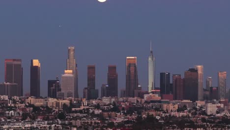 telephoto tilting up aerial shot of the los angeles skyline under a full moon at magic hour in southern california. 4k