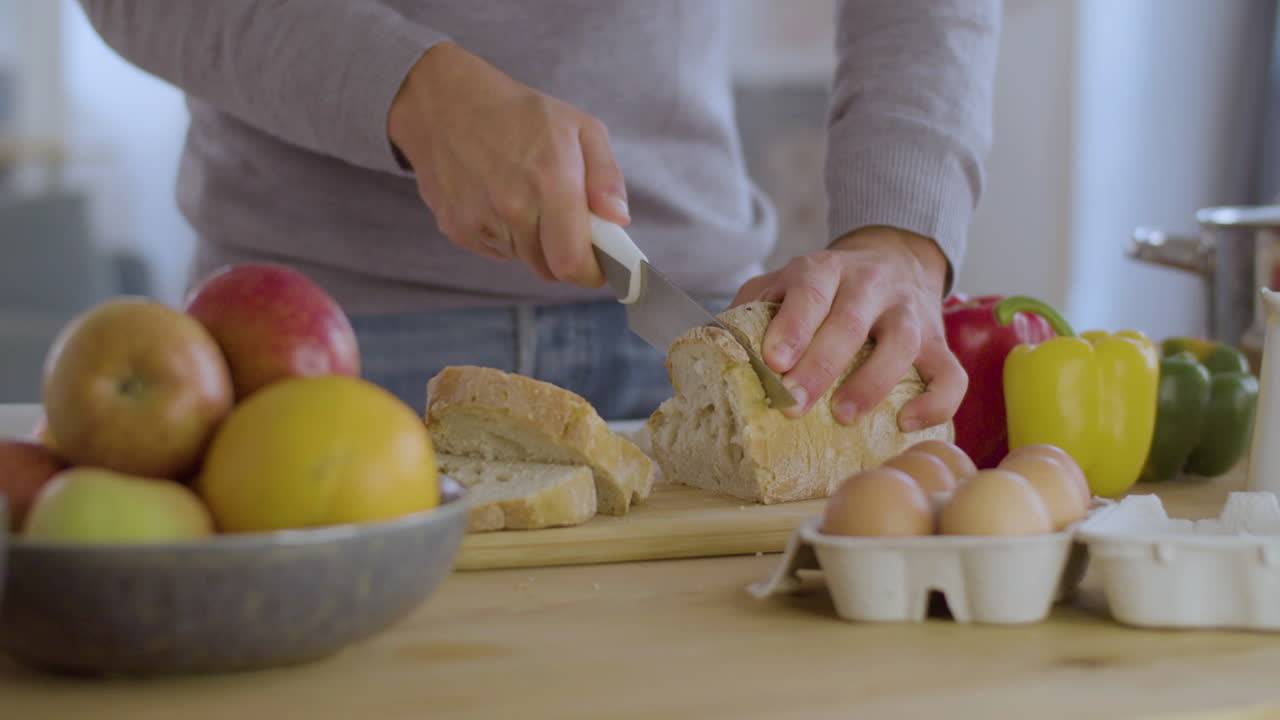 Closeup of young man in grey sweater slicing white bread.