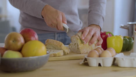 Closeup-of-young-man-in-grey-sweater-slicing-white-bread.