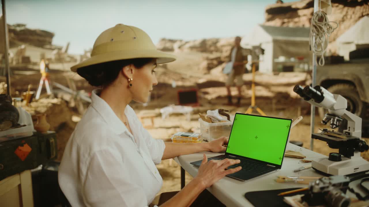 sitio de excavación arqueológica: arqueóloga femenina usando pantalla verde croma clave pantalla portátil, analizando restos fósiles, artefactos de la cultura de la antigua civilización. los historiadores trabajan en el sitio de escavación