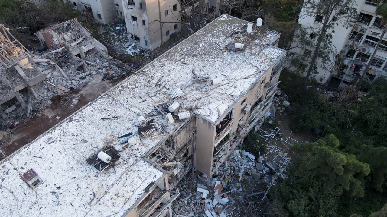 Drone shot over damaged buildings in Tel Aviv. Rubble and collapsed trees are visible after Iranian missile strikes.