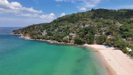 las imágenes de drones capturan una serena playa de phuket con aguas turquesas y vegetación exuberante, mostrando villas de lujo bajo la brillante luz del día
