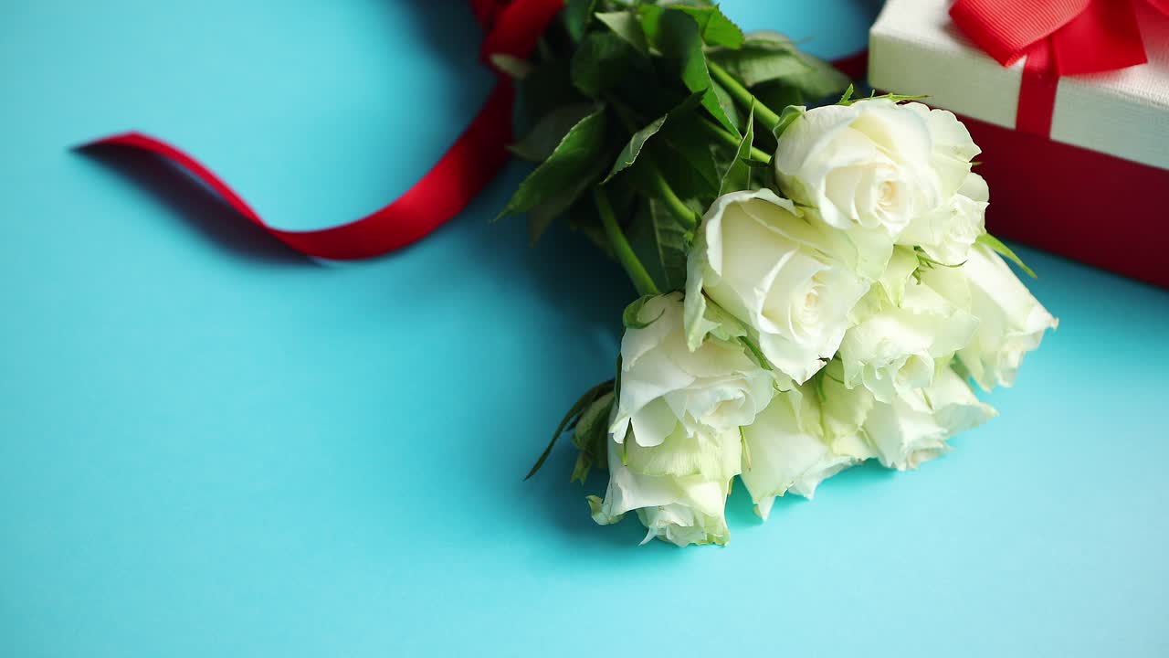 측면에 파란색 배경 박스형 선물에 붉은 활과 흰 장미 꽃다발