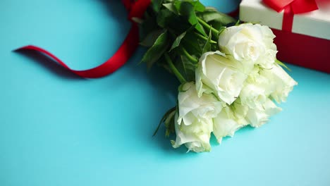Bouquet-of-white-roses-with-red-bow-on-blue-background--Boxed-gift-on-side