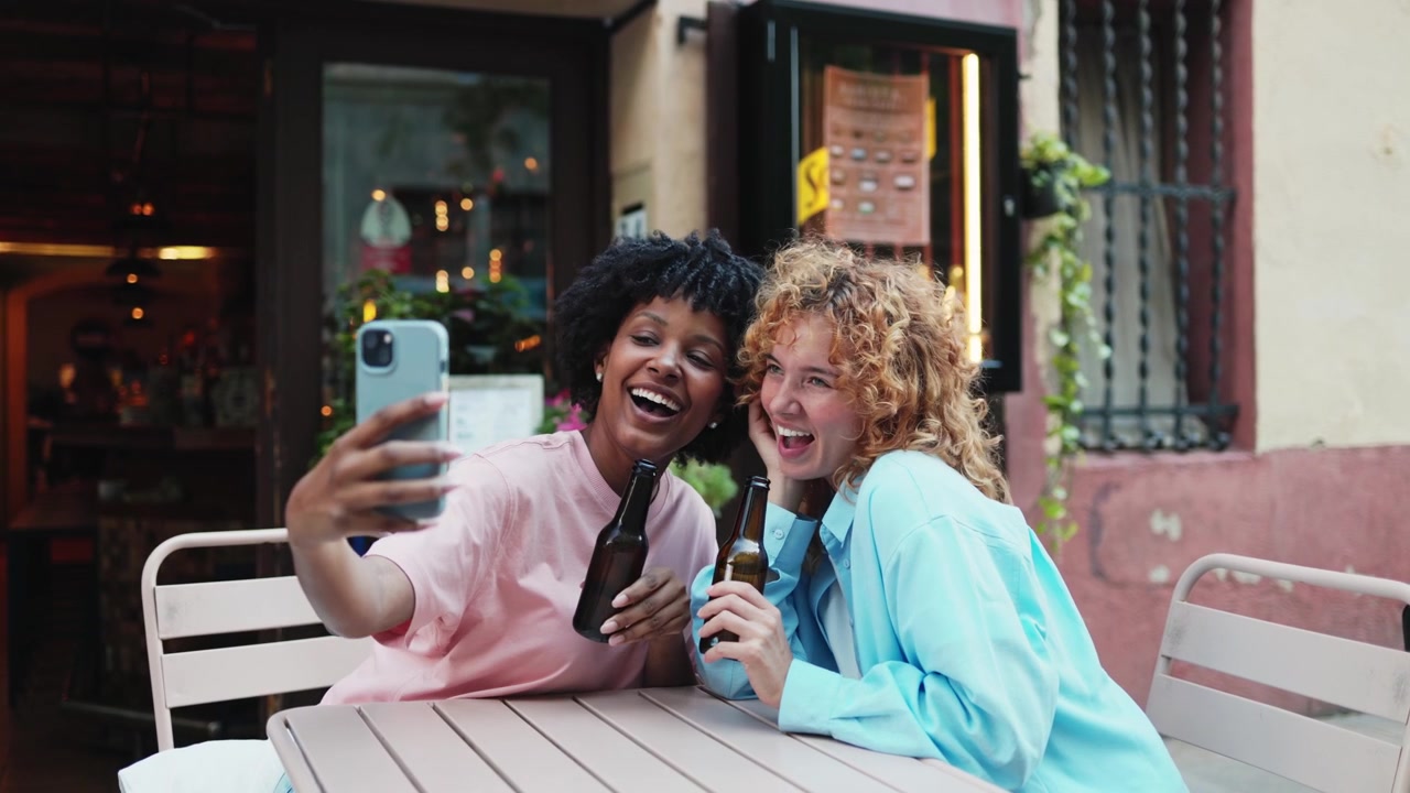 Giovani donne felici che si scattano un selfie con birra in un caffè all'aperto.
