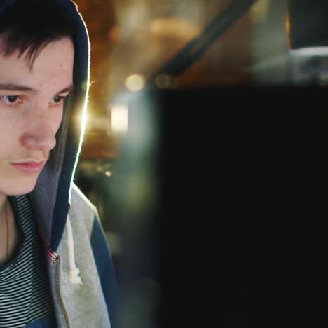 a teenager in a hood sits in front of a computer monitor in the dark 2