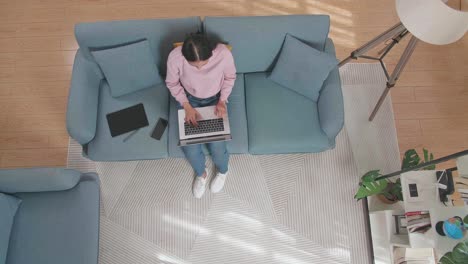vista superior de una mujer escribiendo en una computadora portátil mientras está sentada en el sofá en casa