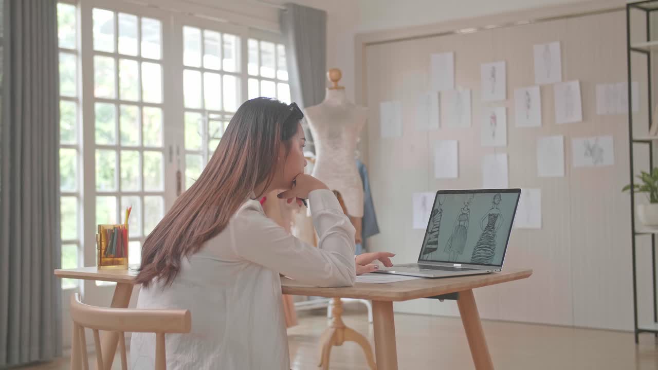 Female Designer Looking At Desk On Laptop Computer And Sketching