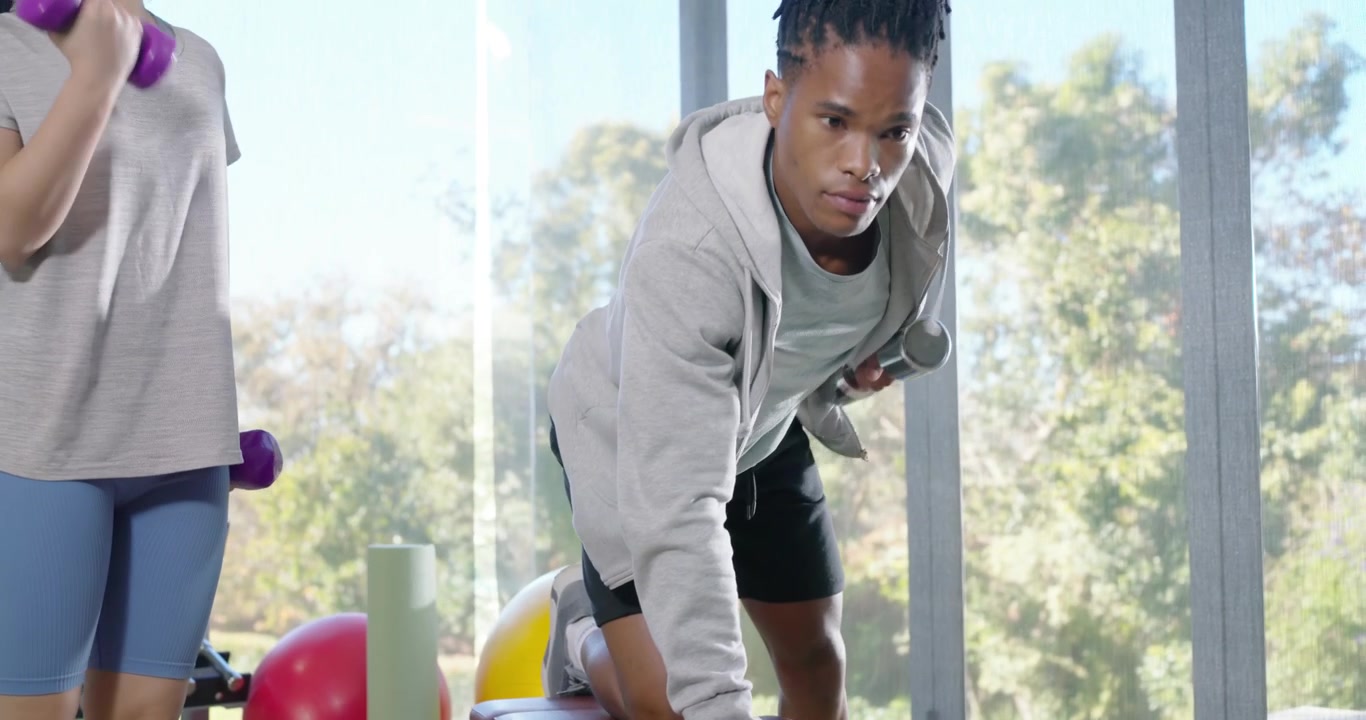 African American duo in gym, man grabbing silver weight, woman curling purple weights for strength