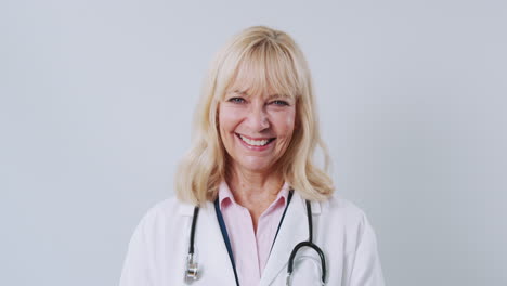 studio shot of mature female doctor wearing white coat against white background smiling at camera